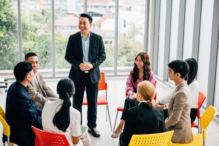 A diverse team of business professionals collaborates in a modern office. They engage in planning, explaining, and presenting, showcasing teamwork, diversity, and confidence in a business meeting